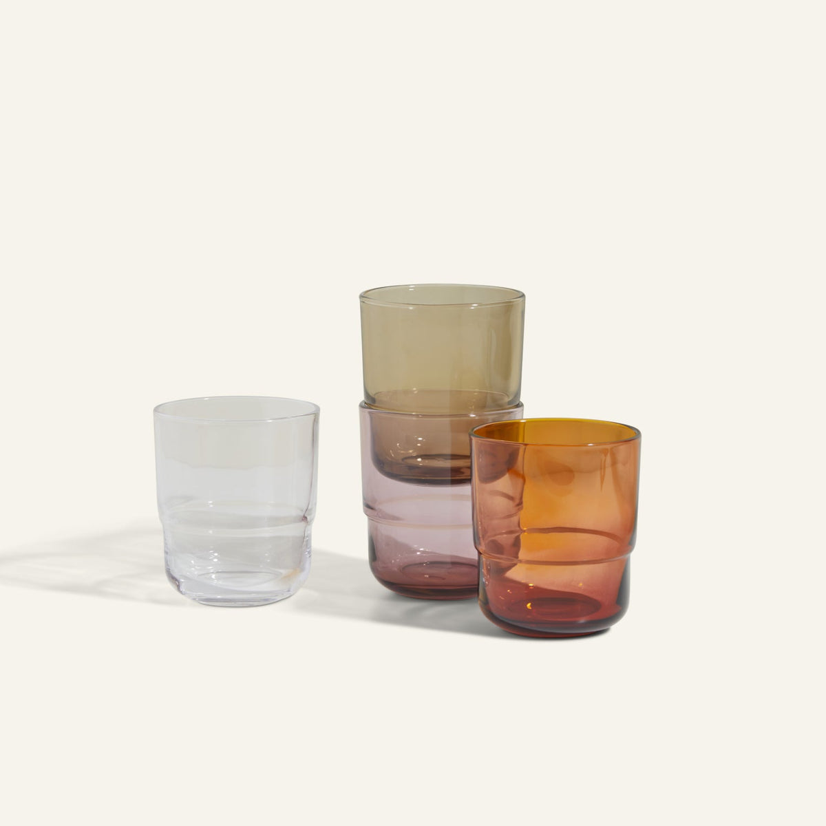 Four handmade Short Night + Day Glasses in clear, light brown, light purple, and amber are stacked and placed side by side against a plain background.