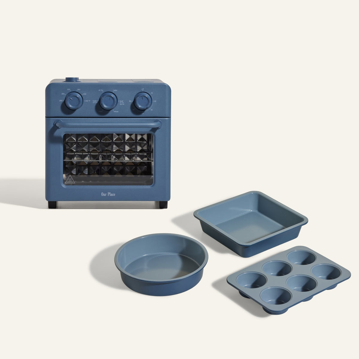 The Wonder Oven + Wonder Oven Baker's Kit is displayed in blue, featuring a countertop oven with matching blue square, round, and six-cup muffin pans on a light background.