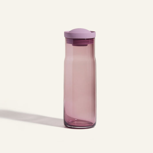 The Night + Day Carafe, a translucent purple water bottle with a matching screw-on lid, stands upright on a plain light background, echoing the sleek silhouette of a modern carafe.