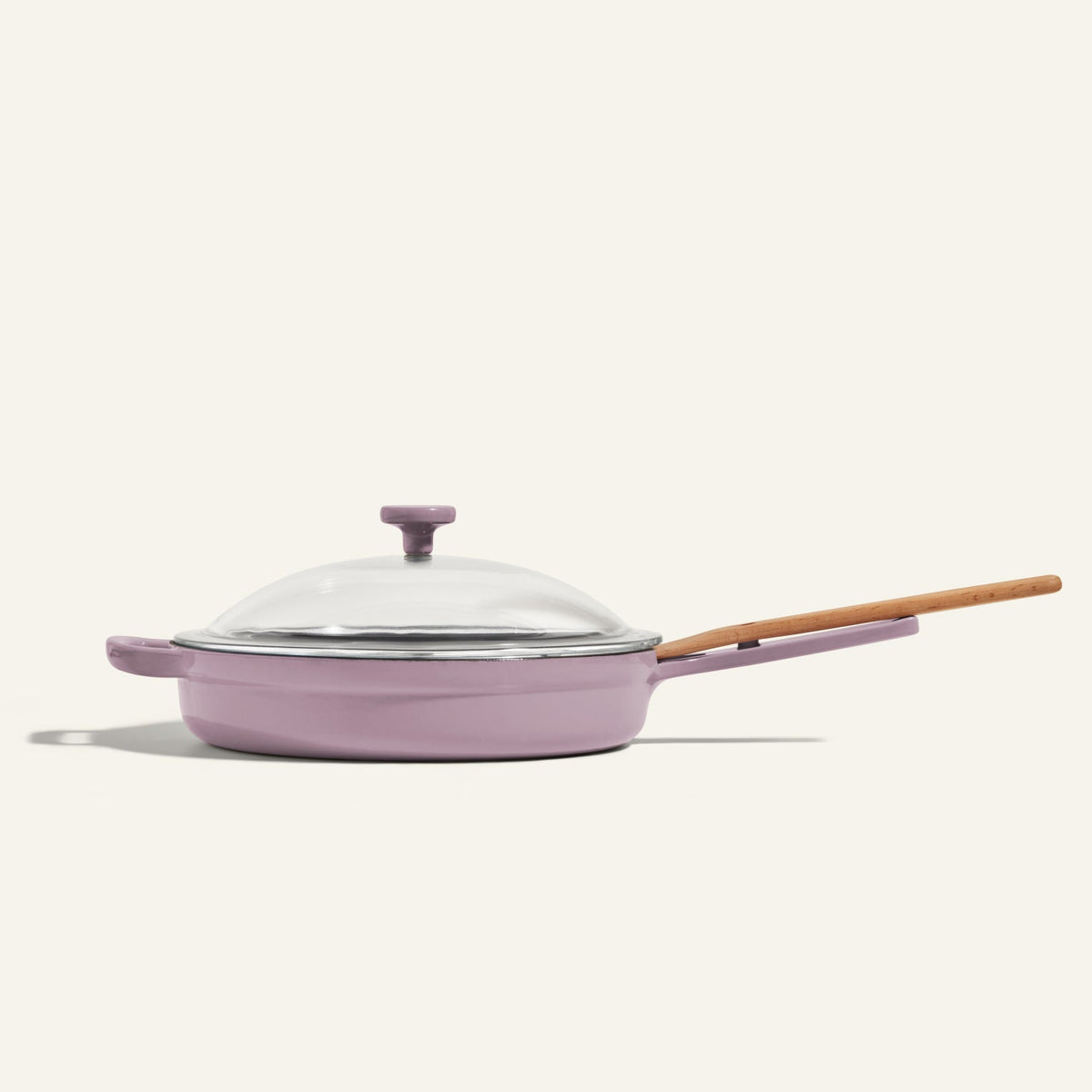 The Cast Iron Always Pan, featuring a light purple enameled finish, nonstick surface, wooden handle, and glass lid, is displayed against a plain off-white background.