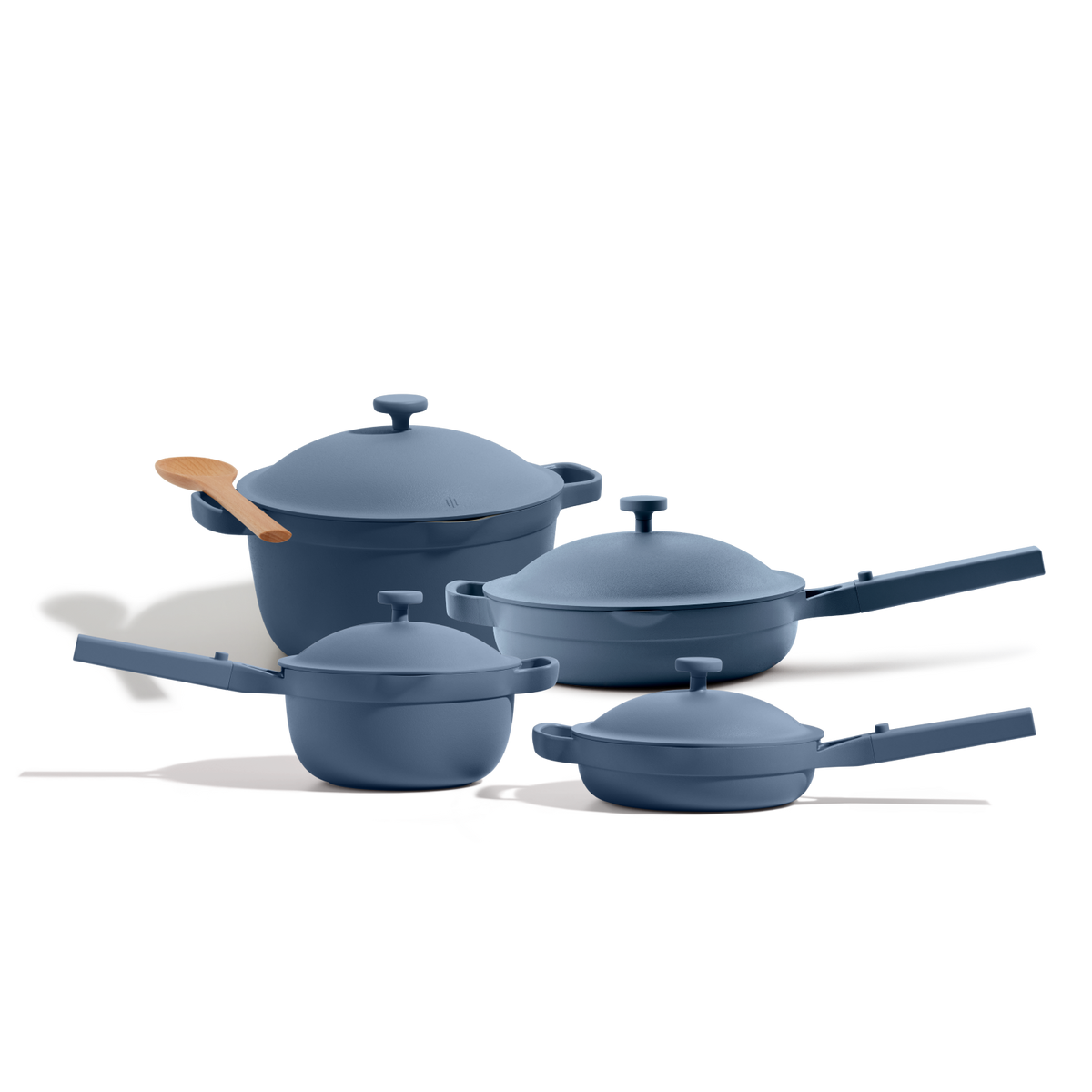 The Cookware Set includes four blue nonstick pieces with lids and a wooden spoon, inspired by the Always Pan’s versatility, shown on a white background.