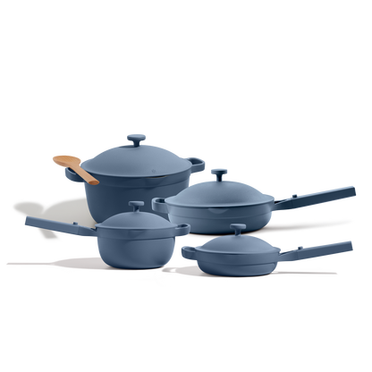 The Cookware Set includes four blue nonstick pieces with lids and a wooden spoon, inspired by the Always Pan’s versatility, shown on a white background.