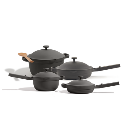 The Cookware Set includes four black nonstick pieces inspired by the Perfect Pot—two saucepans, a deep pan, and a pot—with lids, handles, and a wooden spoon, all arranged on a white background.