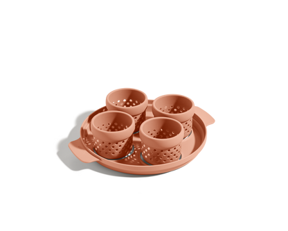 The Egg Poacher features four terra-cotta-colored silicone cups with holes in a matching round tray, ideal for making poached eggs, displayed on a plain white background.