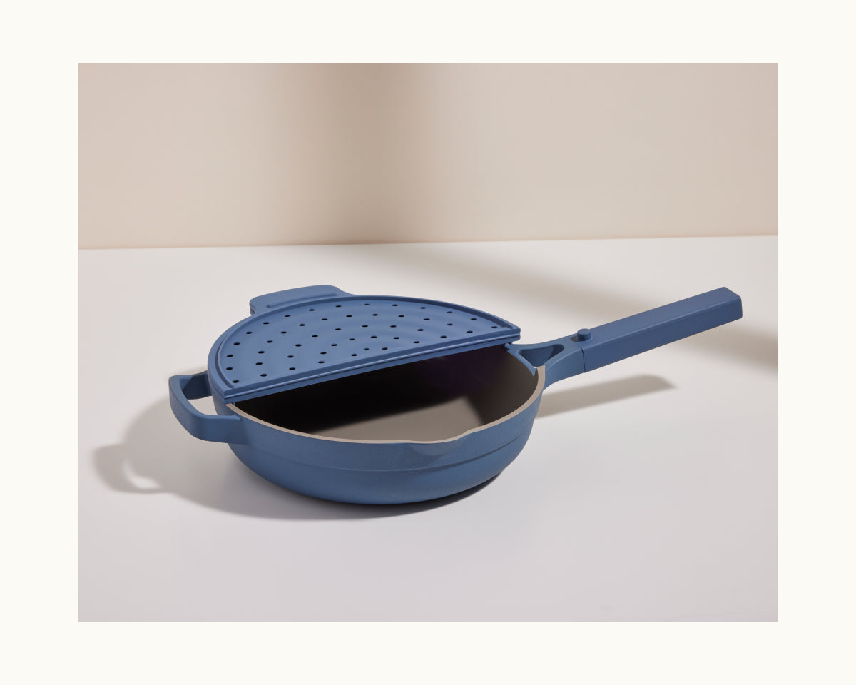 The Fearless Fry is a blue nonstick frying pan with a matching handle, two side handles for easy grip, and a perforated lid for splatter prevention, shown on a plain white background.