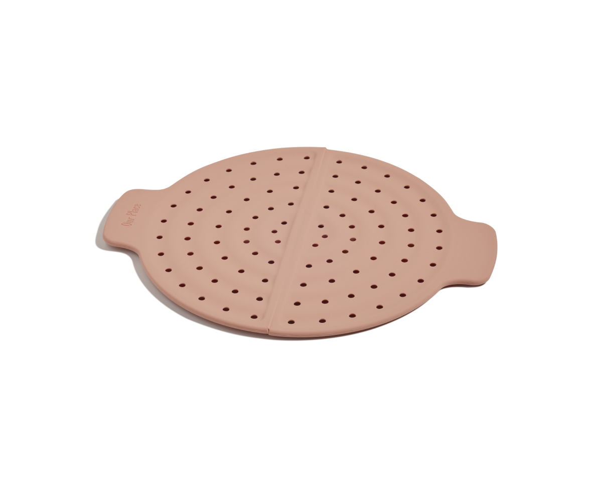 The Fearless Fry is a round pink silicone steamer basket with small holes and two side handles—ideal for splatter prevention in your Always Pan.