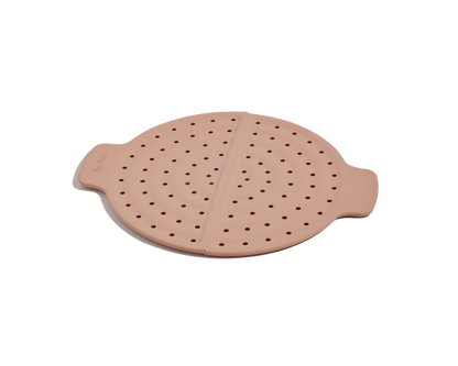 The Fearless Fry is a round pink silicone steamer basket with small holes and two side handles—ideal for splatter prevention in your Always Pan.