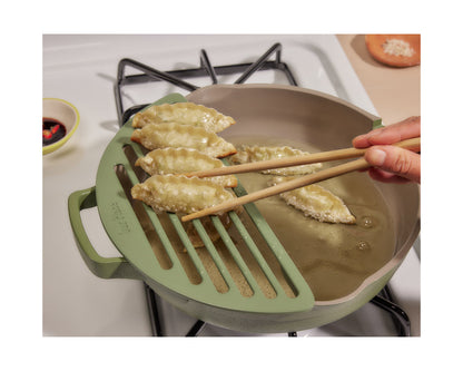 A hand uses chopsticks to lift cooked dumplings from hot oil in a pan equipped with the Fry Deck strainer on a stovetop.