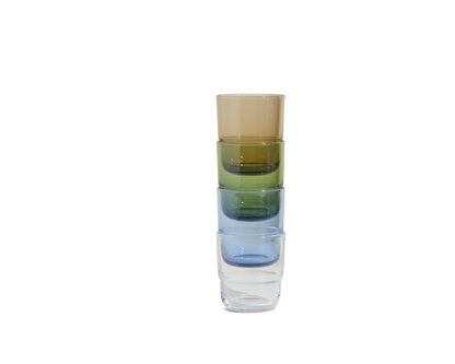 A stack of four Short Night + Day Glasses—brown, green, blue, and clear—made from recycled glass tumblers, arranged vertically on a plain white background.