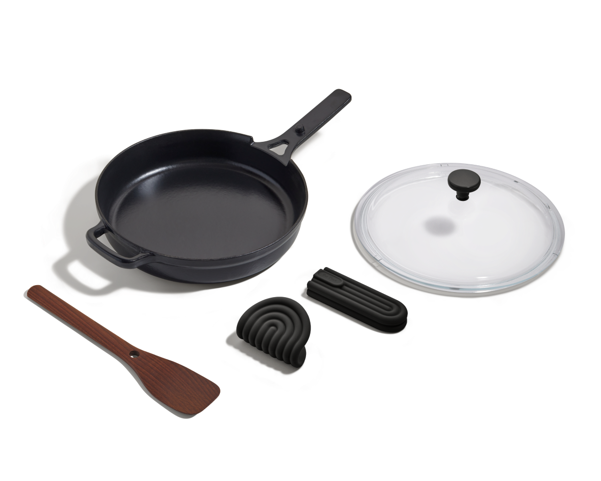 The Cast Iron Always Pan features a long handle, glass lid, wooden spatula, silicone trivet, and foldable black handle cover for 8-in-1 versatility—all shown on a white background.