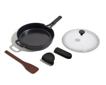 The Cast Iron Always Pan features a long handle, glass lid, wooden spatula, silicone trivet, and foldable black handle cover for 8-in-1 versatility—all shown on a white background.
