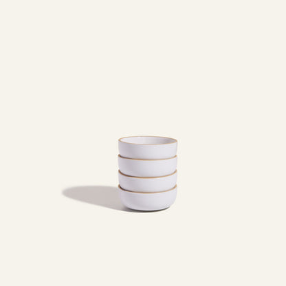 Four white Tiny Bowls, noted for their scratch-resistant ceramic finish, are stacked on a plain light background with a soft left shadow. These durable bowls are ideal as stylish and space-saving stackable tableware.