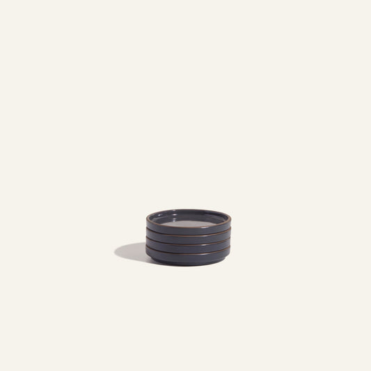 A stack of four Tiny Plates—small, round ceramic snack plates—rests on a light, plain background, perfect for any tableware set.