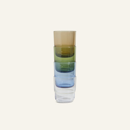 The Short Night + Day Glasses set features four vibrant handmade tumblers in brown, green, blue, and clear—crafted from recycled glass and stacked vertically against a simple light background.