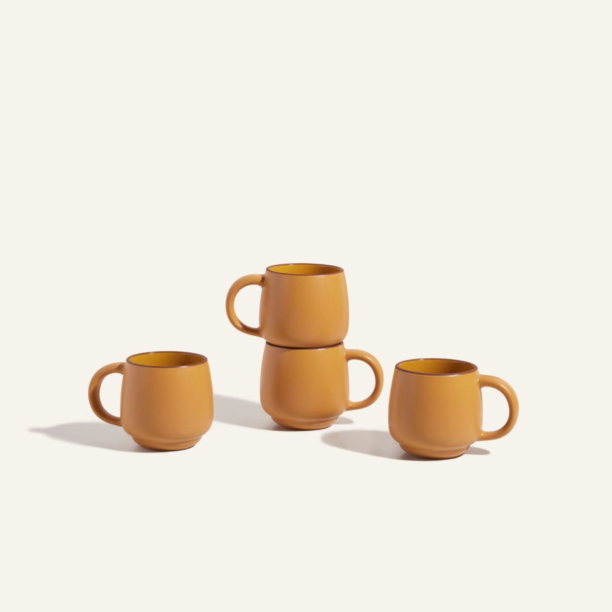 Four Night + Day Mugs in matte orange ceramic stoneware, with two mugs stacked atop each other, set against a light background.