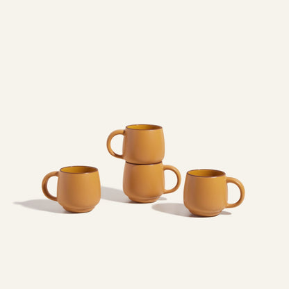 Four Night + Day Mugs in matte orange ceramic stoneware, with two mugs stacked atop each other, set against a light background.