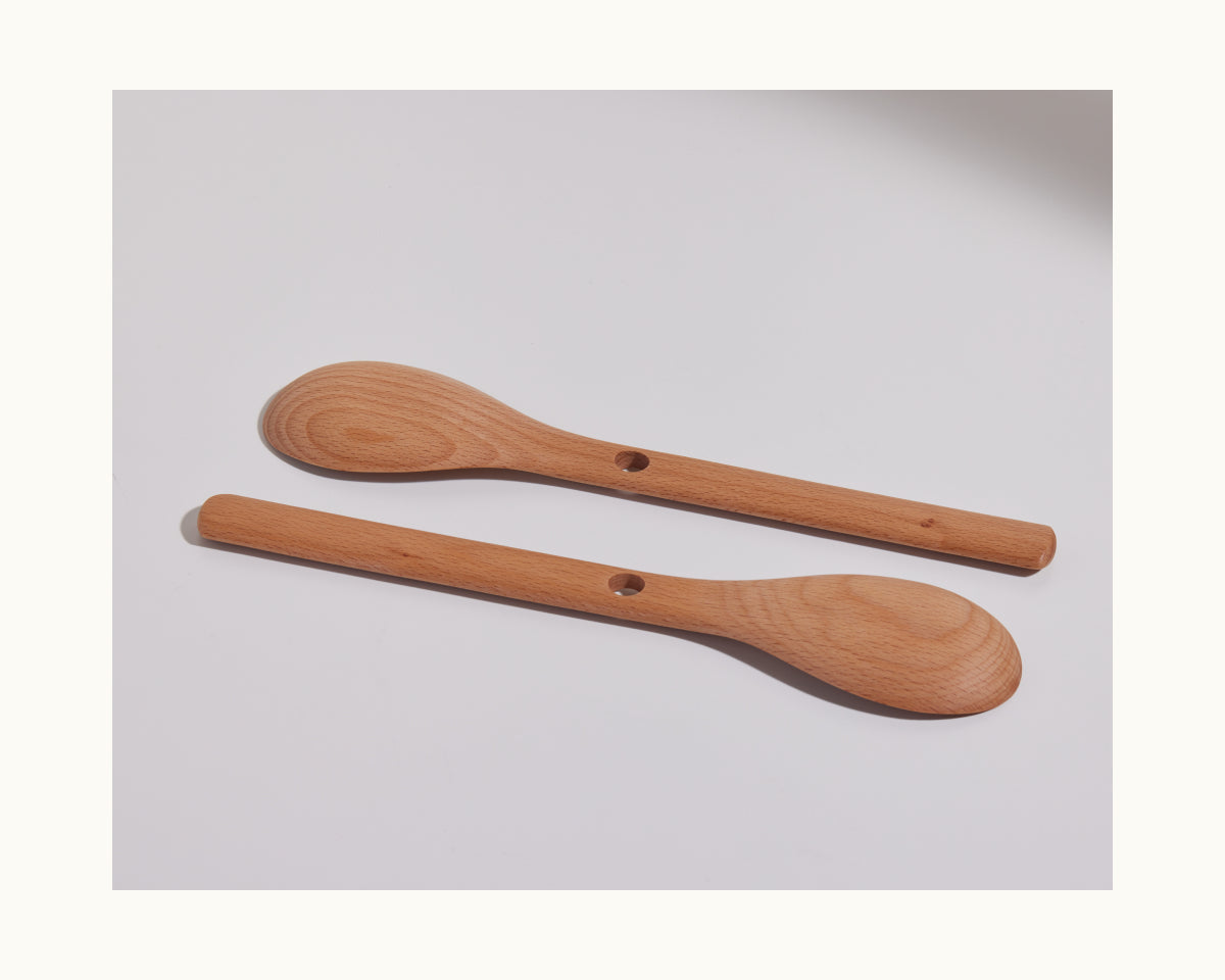 Two Beechwood Spoons with holes in the handles are placed parallel on a plain white surface, highlighting these elegant kitchen utensils for everyday use.