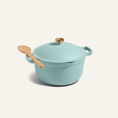 The Perfect Pot in light blue features 8-in-1 nonstick functionality with a lid and gold knob, paired with a wooden spoon on top, displayed against an off-white background.
