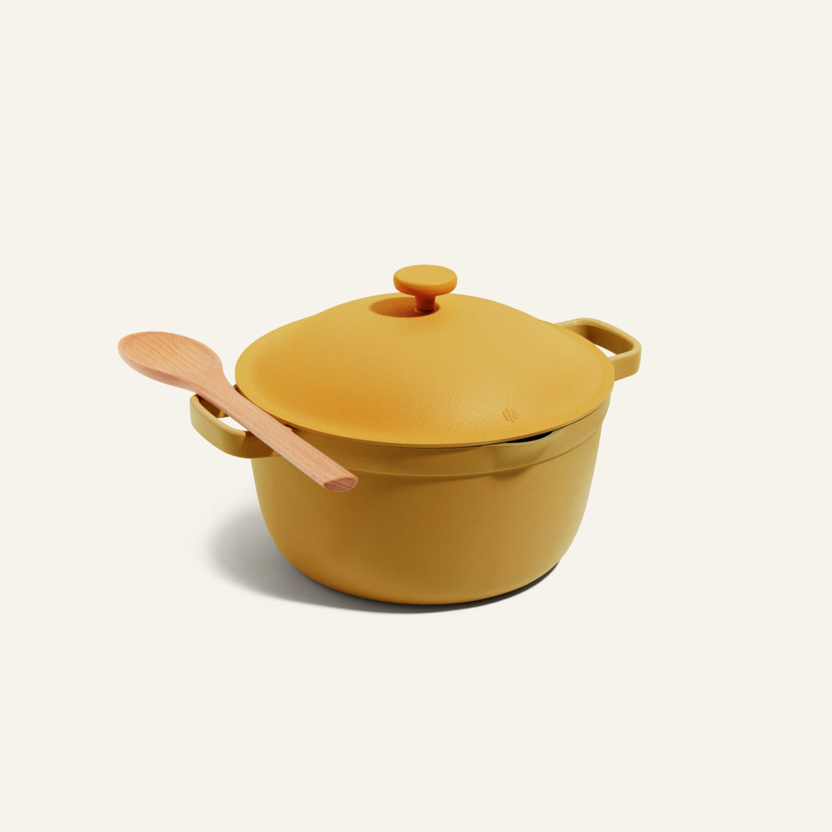 The Perfect Pot, a yellow Dutch oven with handles, sits on a light background. Its sturdy, family-sized design is ideal for stovetop-to-oven meals, while a wooden spoon rests diagonally across the lid, ready for your next creation.