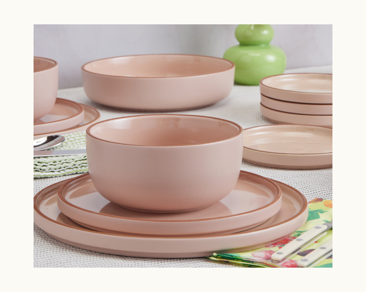 Pink ceramic Soup Bowls and plates from a stylish set are arranged with cutlery and a green decorative item, perfect for elevating your tableware collection.