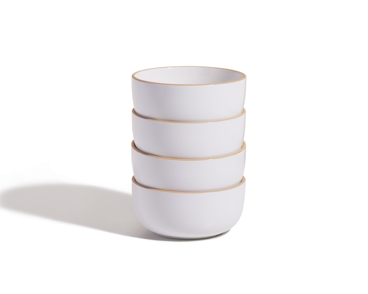 A stack of four white Soup Bowls with thin gold rims, part of an elegant ceramic set, sits on a plain white surface with a soft shadow to the left.