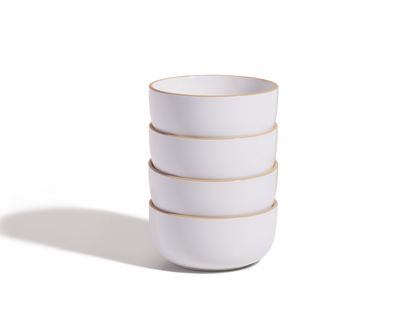 A stack of four white Soup Bowls with thin gold rims, part of an elegant ceramic set, sits on a plain white surface with a soft shadow to the left.