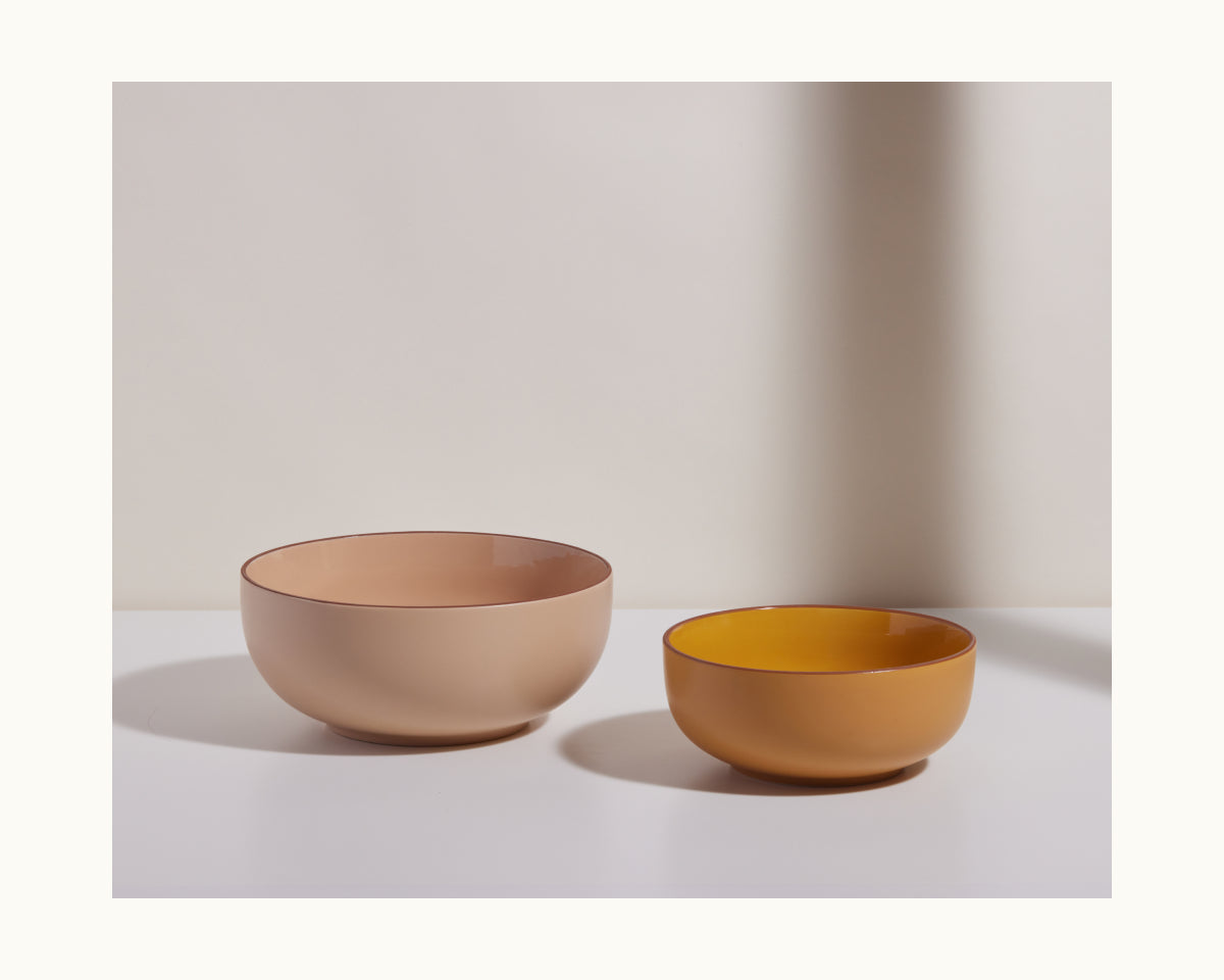 Two stackable Serving Bowls—one large in beige and one small in mustard yellow—are displayed side by side on a white surface with a neutral background.