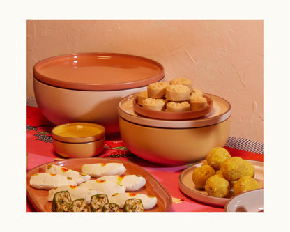 Serving Bowls filled with assorted baked and rolled snacks are stacked on a red tablecloth, displayed in front of a peach-colored wall.