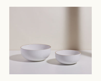 Set of two white Serving Bowls in different sizes, featuring a subtle gold rim and a stackable design, displayed on a white surface with a neutral background—an elegant addition to any kitchen tableware collection.