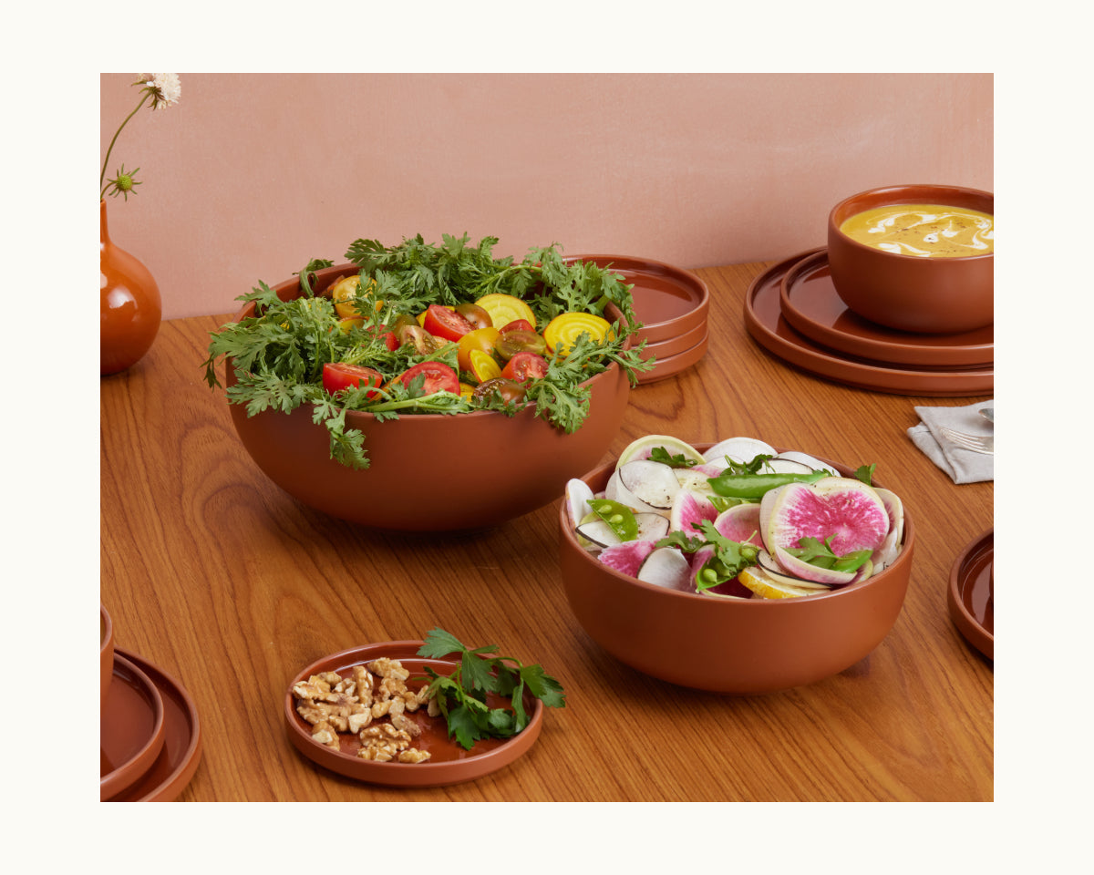 Serving Bowls filled with mixed vegetable salad, radish salad, walnuts, herbs, and creamy yellow soup create a vibrant spread on a wooden table.