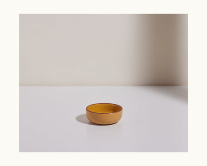 Tiny Bowls are small, round, brown ceramic dishes perfect for any setting. Stackable and stylish, they sit beautifully on a white surface against a light wall with soft shadows—ideal tableware for versatile use.