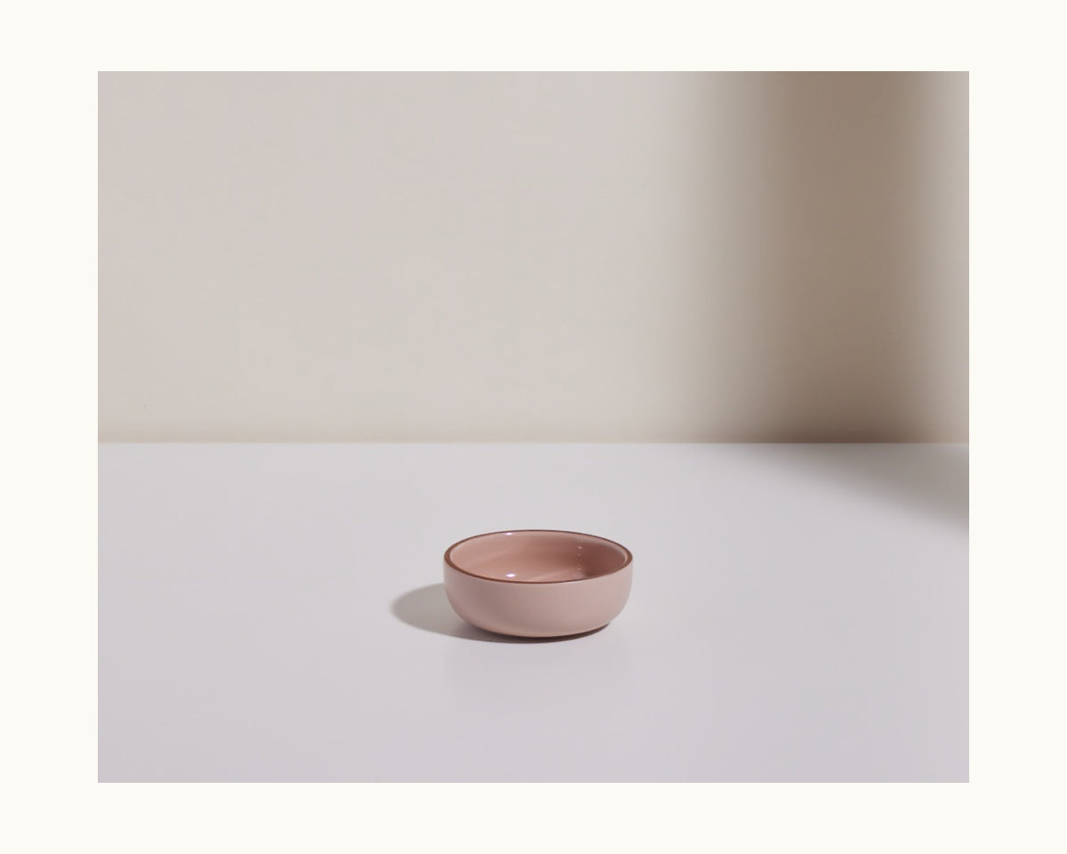 A small, empty pink Tiny Bowl sits on a white surface against a plain, light background—ideal for anyone seeking scratch-resistant, stackable tableware.