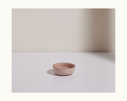 A small, empty pink Tiny Bowl sits on a white surface against a plain, light background—ideal for anyone seeking scratch-resistant, stackable tableware.