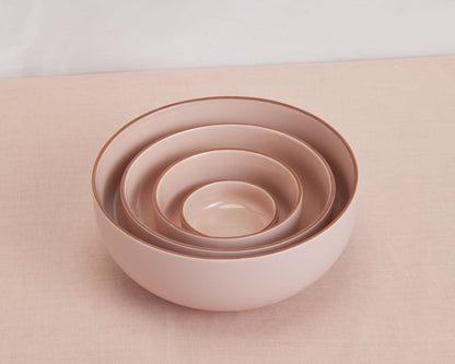 Four Tiny Bowls of different sizes are stacked on a light pink fabric surface, highlighting elegant, stackable tableware for stylish organization.