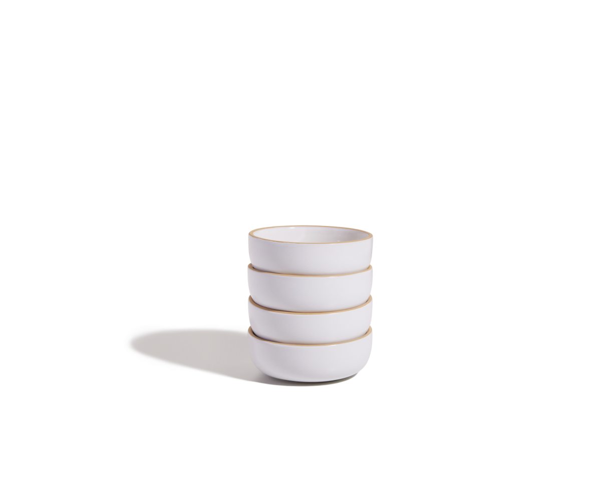 A stack of four Tiny Bowls, white ceramic with light brown rims and scratch-resistant surfaces, is shown on a plain white background with a shadow to the left.