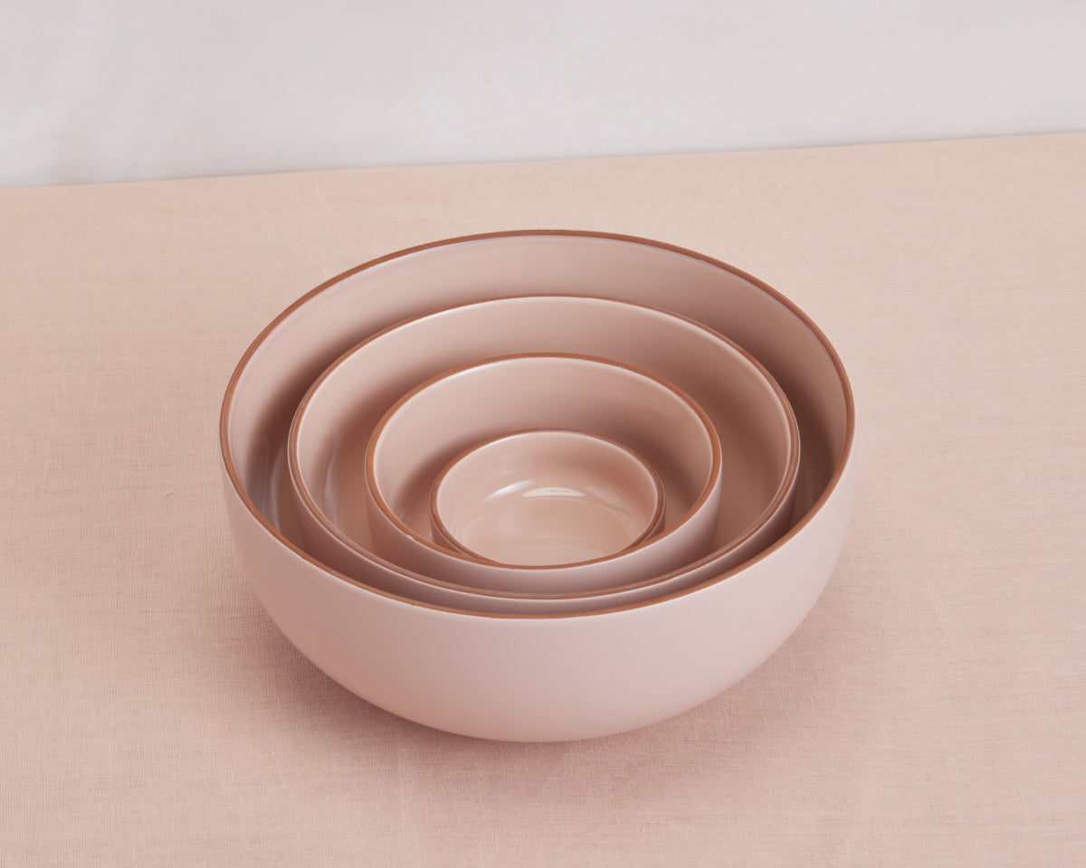 Four nesting Tiny Bowls in pink ceramic, each a different size, are stacked together on a light pink fabric surface, highlighting elegant and scratch-resistant stackable tableware.