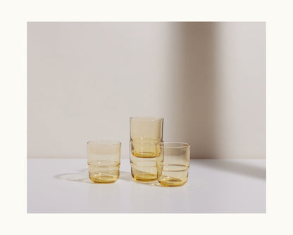 Three Short Night + Day Glasses, handmade in amber and stacked on a white surface with a light background, highlight the colorful elegance of these unique tumblers.