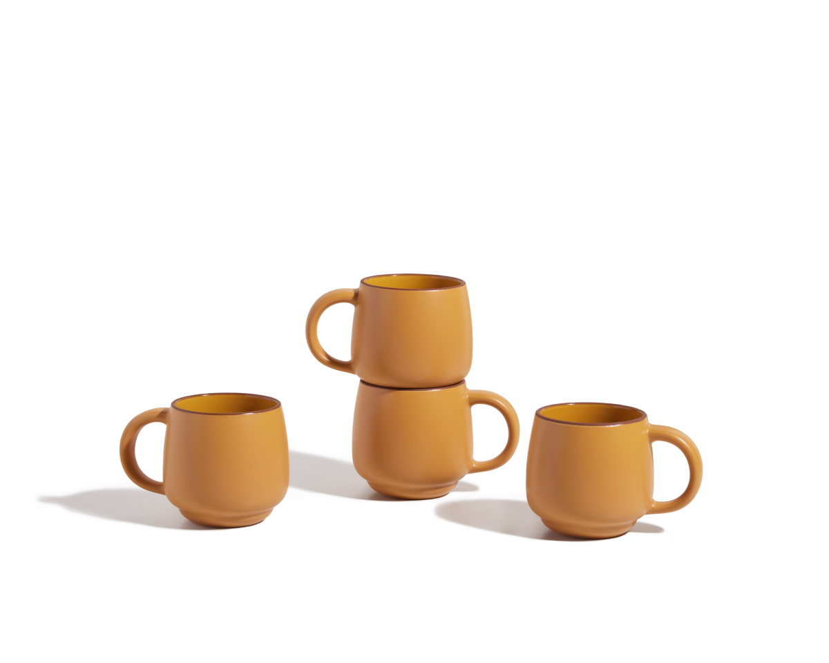 Four Night + Day Mugs in matte orange ceramic stoneware are displayed on a white surface; two mugs are stacked while the other two sit side by side, highlighting their stackable design and ample capacity.
