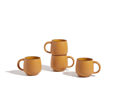 Four Night + Day Mugs in matte orange ceramic stoneware are displayed on a white surface; two mugs are stacked while the other two sit side by side, highlighting their stackable design and ample capacity.