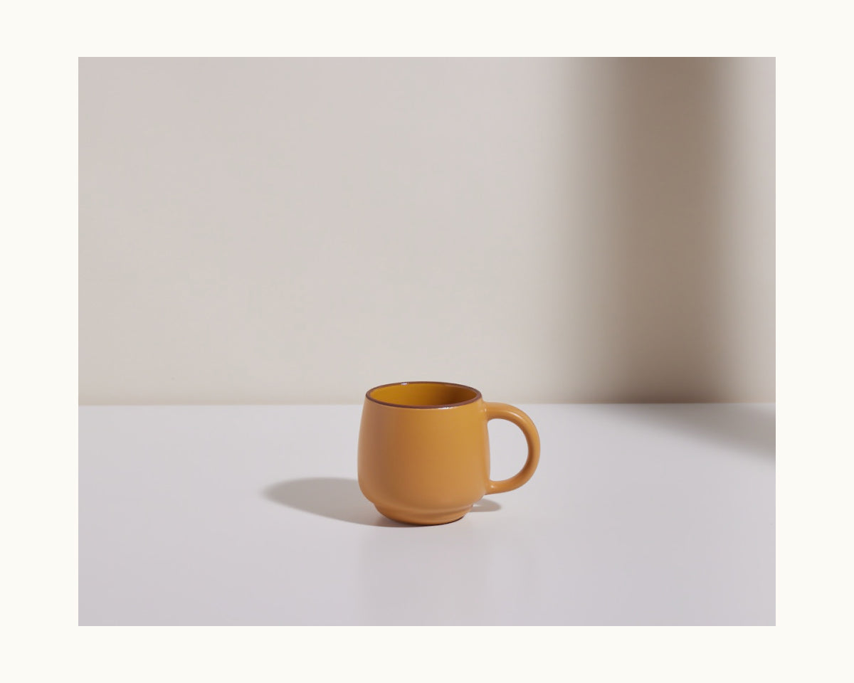 A Night + Day Mug in plain yellow ceramic stoneware sits on a white surface against a light background, its generous capacity highlighted as it casts a shadow to its left.