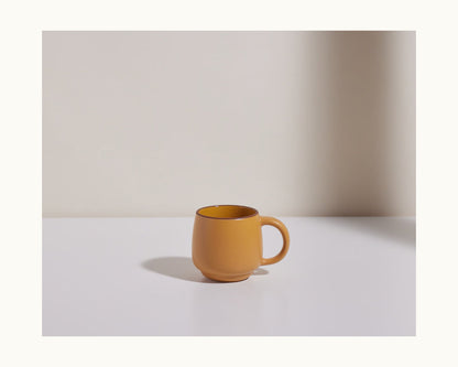 A Night + Day Mug in plain yellow ceramic stoneware sits on a white surface against a light background, its generous capacity highlighted as it casts a shadow to its left.