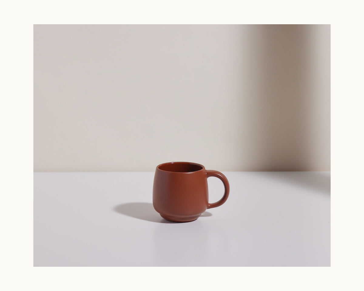 A Night + Day Mug made from brown ceramic stoneware rests on a white surface with a neutral background, casting a soft shadow to the left.