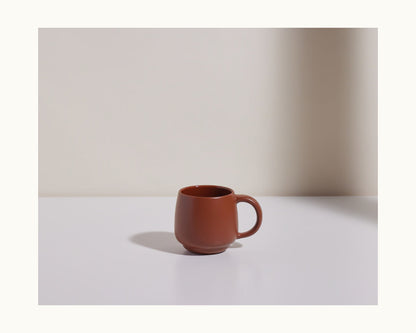 A Night + Day Mug made from brown ceramic stoneware rests on a white surface with a neutral background, casting a soft shadow to the left.