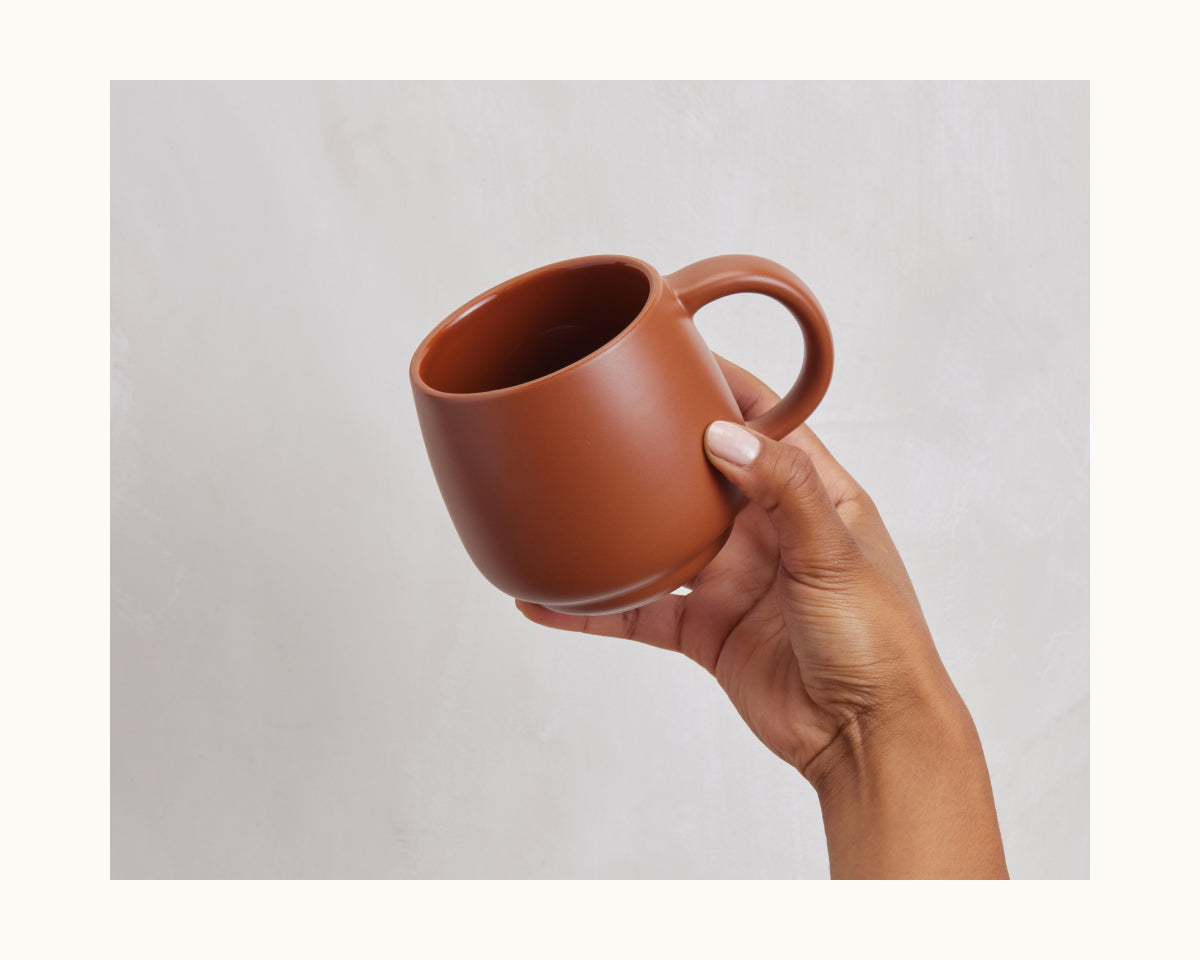A hand holds a large, empty Night + Day Mug with generous capacity against a light gray background.