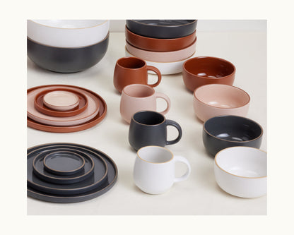 Night + Day Mugs: Stackable ceramic stoneware mugs in white, black, terracotta, and blush colors arranged on a light surface.
