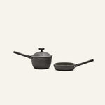 The Tiny Cookware Duo, featuring a black saucepan with lid and a matching black frying pan, are placed side by side against a plain light background.