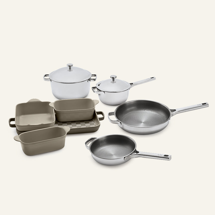 The Titanium Pro Cookware + Bakeware Set 2.0 includes stainless steel pots and pans with lids, alongside several rectangular, light brown ceramic bakeware dishes.