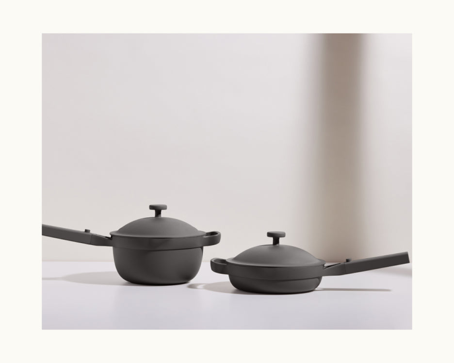 The Cookware Set, featuring two matte black pieces each with a lid and long handle, is displayed on a white surface against a light background.