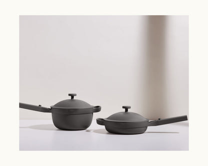 The Cookware Set, featuring two matte black pieces each with a lid and long handle, is displayed on a white surface against a light background.