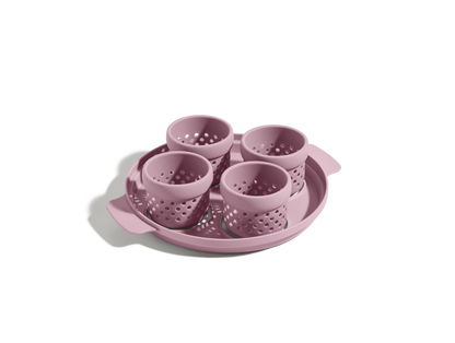 The Egg Poacher includes four pink silicone cups on a matching round tray with handles, ideal for making poached eggs, displayed on a white background.